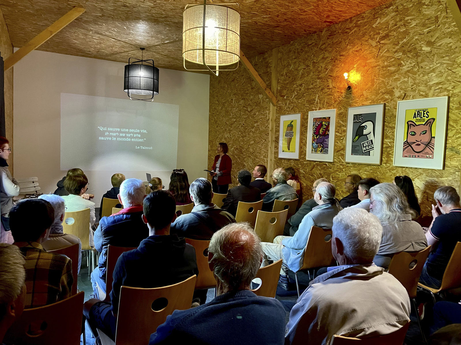Public assis pendant une conférence projetée dans la salle en bois de Maison Farouche